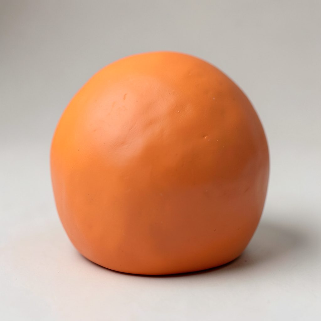 Soft clay-model portrait of a rounded figure with warm orange head and teal shoulders, dark backdrop.